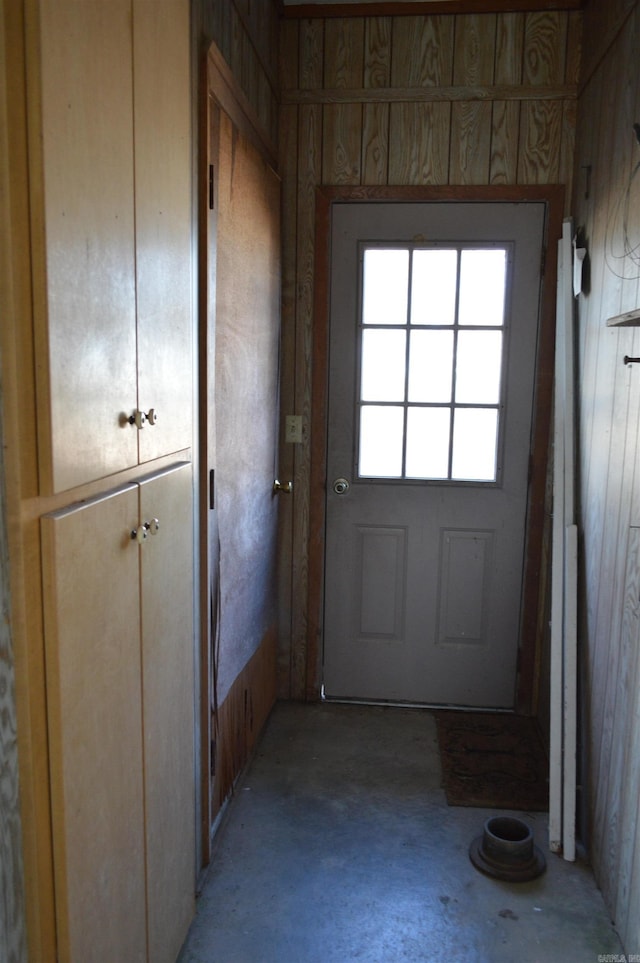 doorway to outside with wooden walls and concrete floors