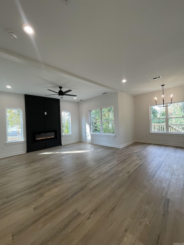 unfurnished living room with ceiling fan with notable chandelier, a large fireplace, light wood-type flooring, and a healthy amount of sunlight