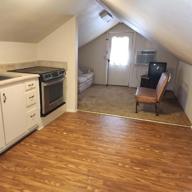 kitchen featuring stainless steel electric range oven, a wall mounted air conditioner, vaulted ceiling, white cabinets, and light wood-type flooring