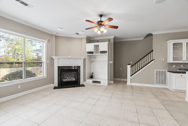 unfurnished living room with ceiling fan, light tile patterned flooring, crown molding, and a high end fireplace