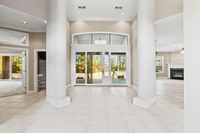 tiled entryway with a high end fireplace, a high ceiling, crown molding, ceiling fan, and ornate columns