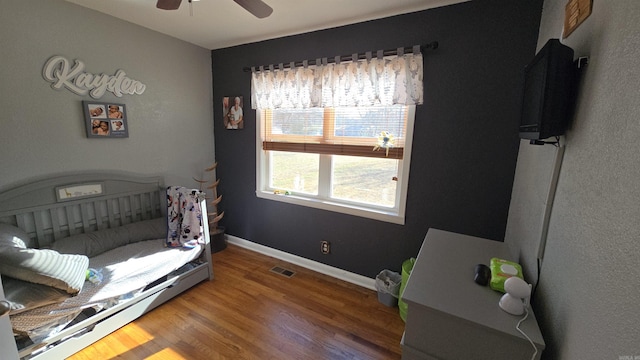 bedroom featuring ceiling fan, a nursery area, and wood-type flooring