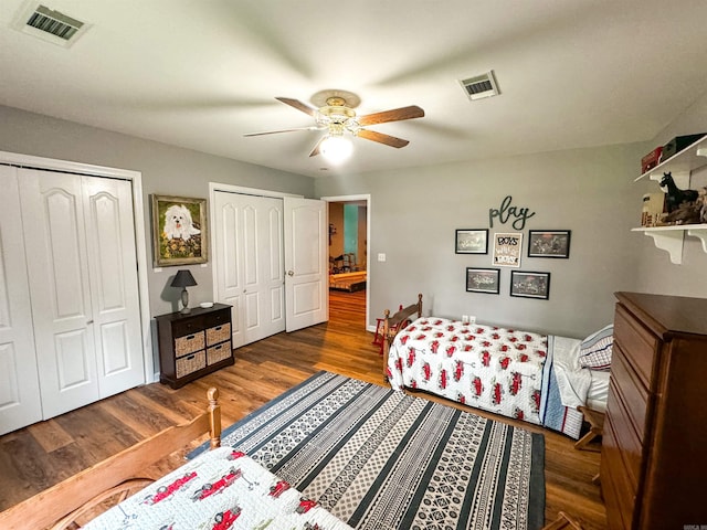 bedroom with dark hardwood / wood-style flooring, two closets, and ceiling fan