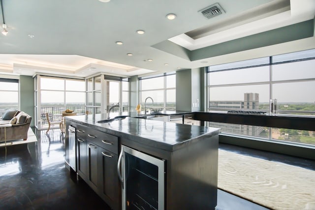 kitchen with a raised ceiling, wine cooler, sink, and an island with sink