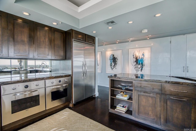 kitchen featuring appliances with stainless steel finishes, dark brown cabinetry, dark wood-type flooring, and dark stone countertops