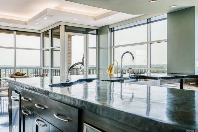 kitchen featuring a raised ceiling, expansive windows, dark stone countertops, and sink