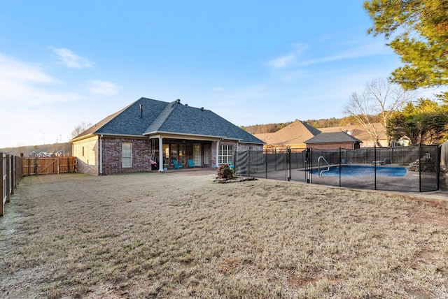 rear view of property featuring a lawn, a patio, and a fenced in pool