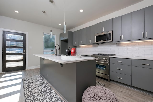 kitchen with appliances with stainless steel finishes, a kitchen breakfast bar, gray cabinetry, hanging light fixtures, and an island with sink