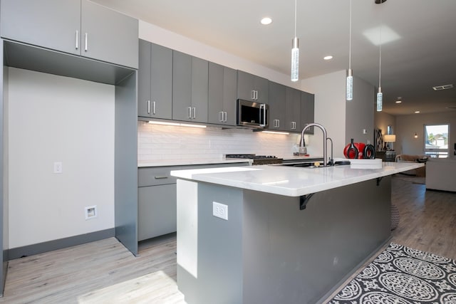 kitchen with gray cabinetry, hanging light fixtures, tasteful backsplash, a breakfast bar area, and a center island with sink