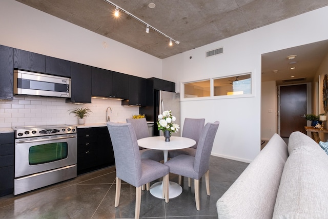 kitchen featuring a towering ceiling, backsplash, appliances with stainless steel finishes, and track lighting