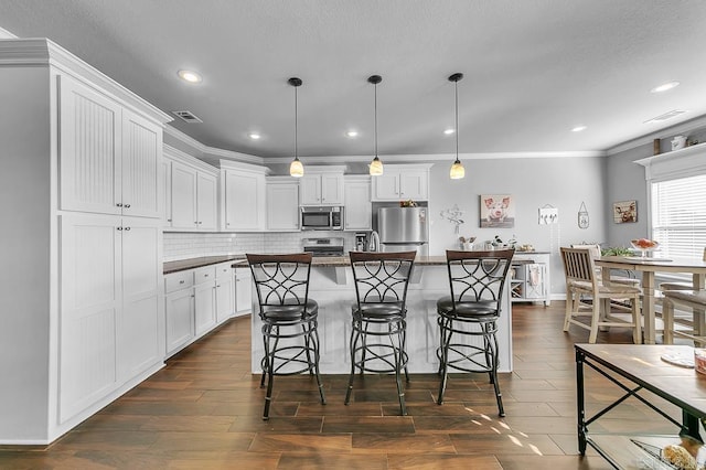 kitchen featuring a kitchen breakfast bar, stainless steel appliances, decorative light fixtures, white cabinets, and a center island