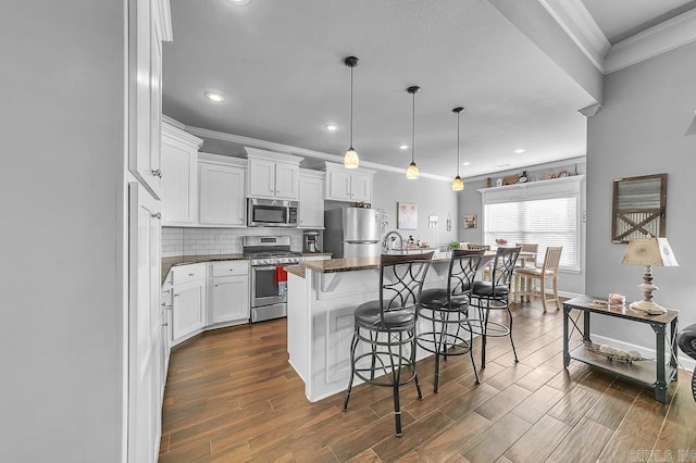 kitchen with decorative backsplash, appliances with stainless steel finishes, a kitchen bar, a center island with sink, and white cabinetry