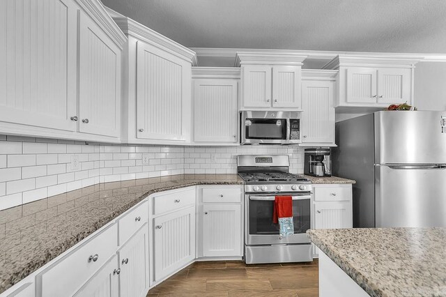 kitchen featuring white cabinetry, dark wood-type flooring, tasteful backsplash, light stone counters, and appliances with stainless steel finishes