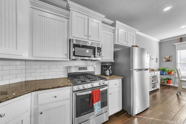 kitchen featuring backsplash, dark stone counters, stainless steel appliances, crown molding, and white cabinets