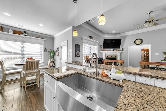 kitchen with white cabinetry, sink, dark stone counters, pendant lighting, and ornamental molding