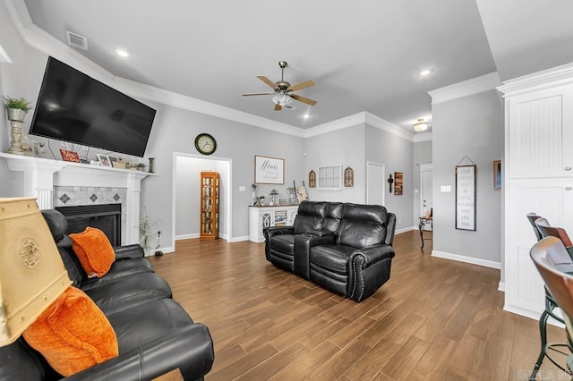 living room featuring hardwood / wood-style floors, ceiling fan, crown molding, and a tiled fireplace