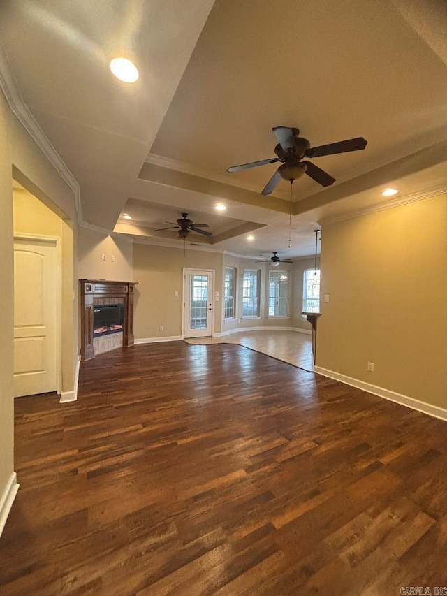 unfurnished living room featuring a tile fireplace, dark hardwood / wood-style flooring, a tray ceiling, and ceiling fan