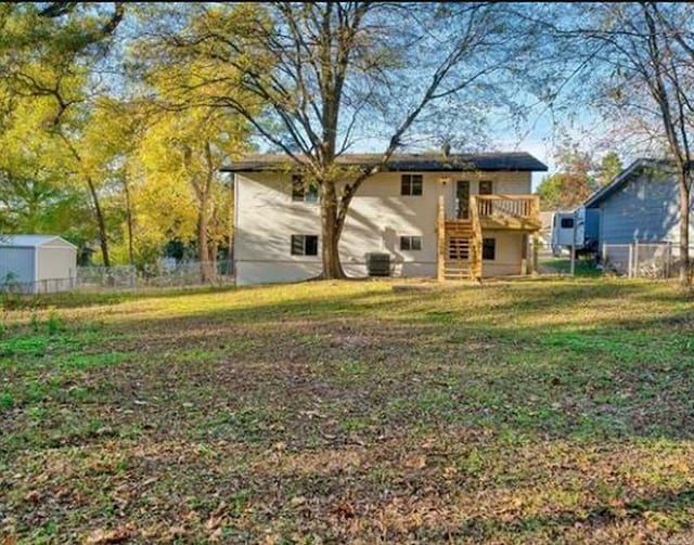 rear view of property featuring a yard, a wooden deck, and central AC