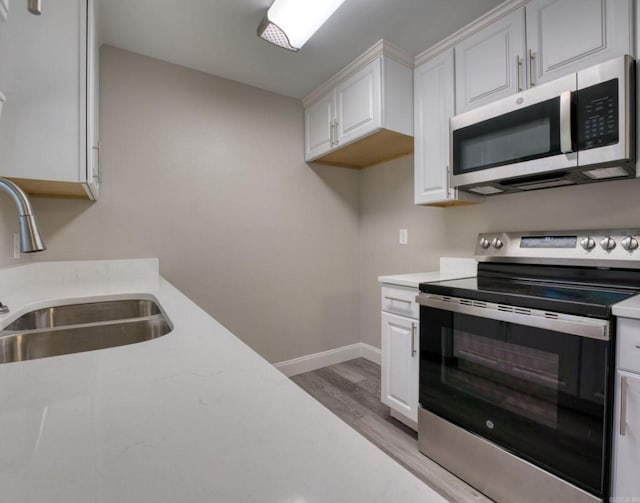 kitchen with sink, white cabinets, light wood-type flooring, and appliances with stainless steel finishes