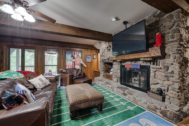 living room featuring beamed ceiling, ceiling fan, a fireplace, and wooden walls