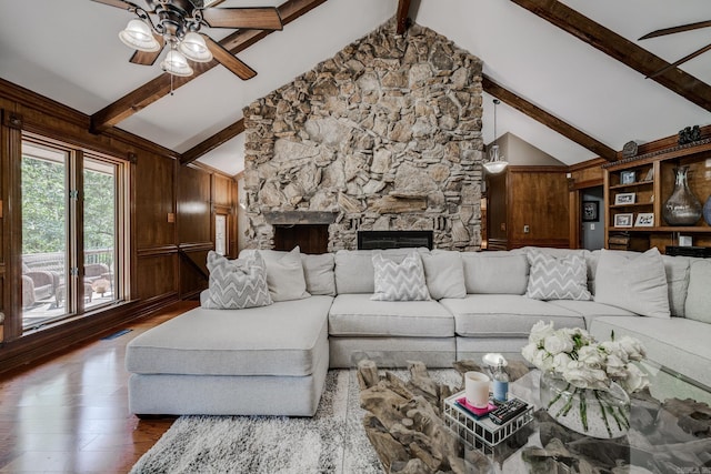 living room with hardwood / wood-style floors, a stone fireplace, wooden walls, vaulted ceiling with beams, and ceiling fan