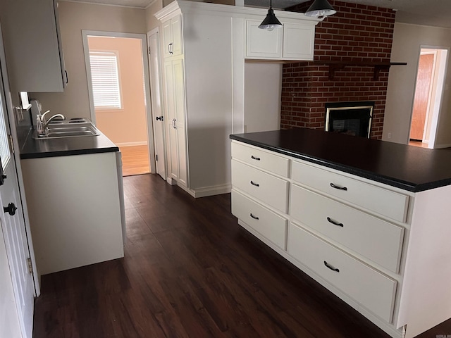 kitchen with dark hardwood / wood-style flooring, white cabinetry, sink, and a brick fireplace