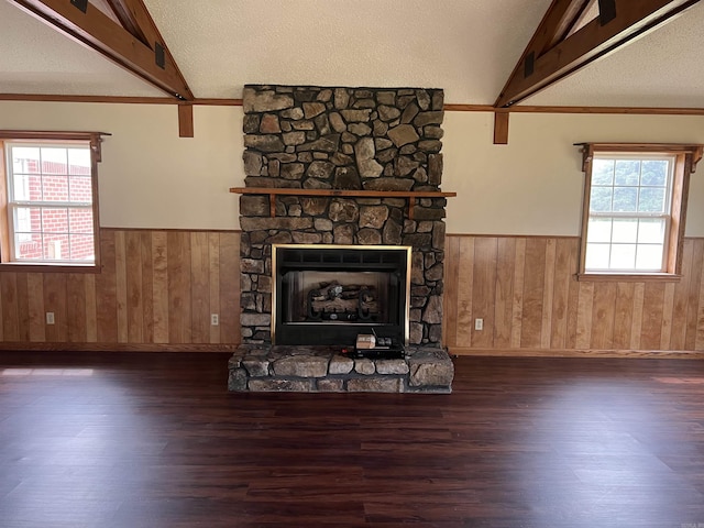 unfurnished living room with a textured ceiling, lofted ceiling with beams, a stone fireplace, and dark wood-type flooring