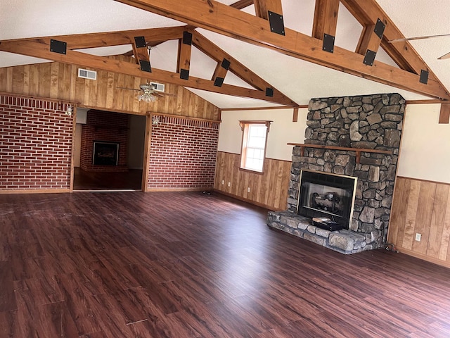 unfurnished living room with a stone fireplace, ceiling fan, brick wall, and vaulted ceiling with beams