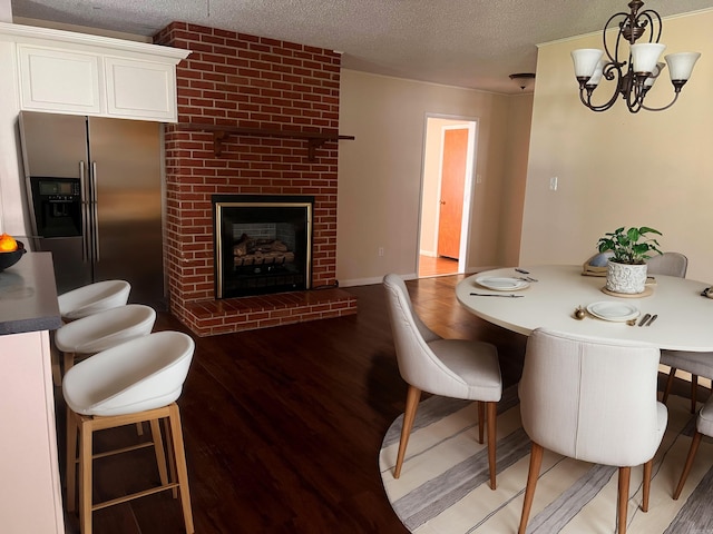 dining room with a textured ceiling, wood-type flooring, a fireplace, and a chandelier