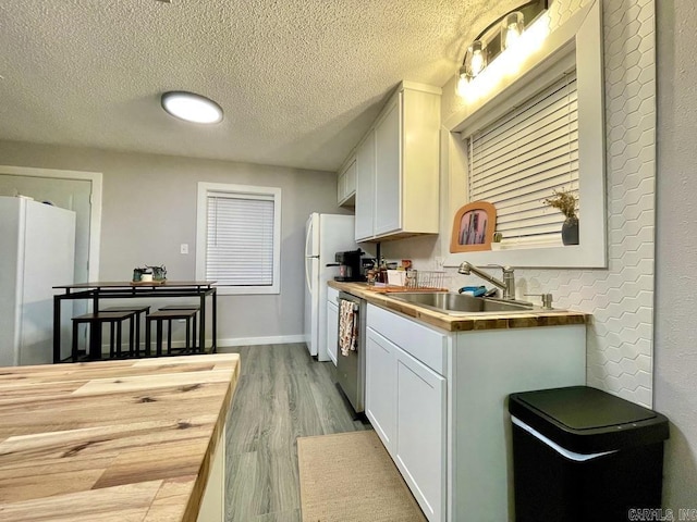 kitchen with stainless steel dishwasher, white refrigerator, white cabinetry, and sink