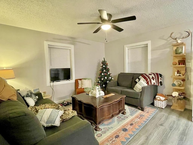 living room with ceiling fan, a textured ceiling, and light wood-type flooring