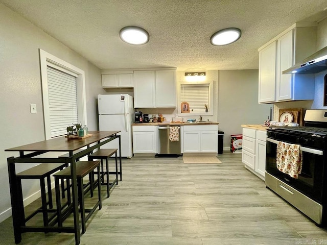 kitchen featuring a textured ceiling, stainless steel appliances, sink, wall chimney range hood, and white cabinets