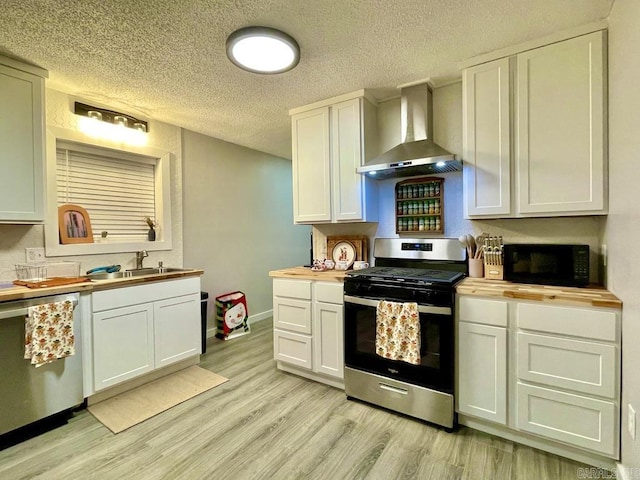 kitchen featuring white cabinets, wall chimney range hood, sink, butcher block countertops, and stainless steel appliances