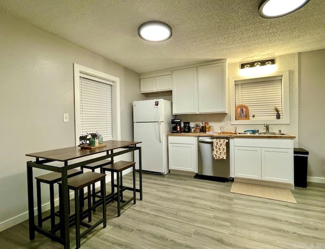 kitchen with sink, stainless steel dishwasher, butcher block countertops, white fridge, and white cabinetry