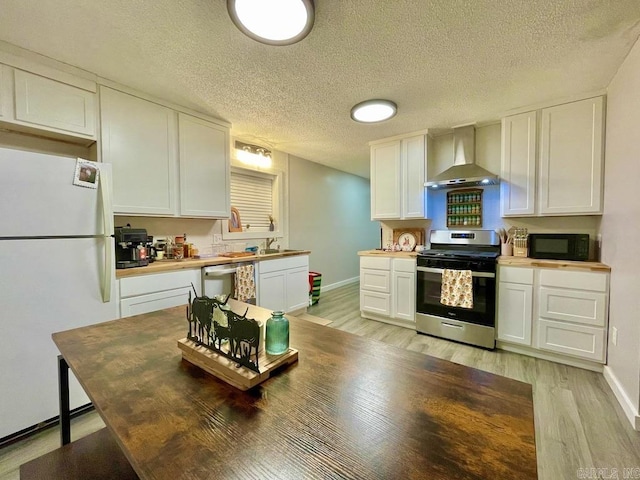 kitchen featuring wall chimney exhaust hood, light hardwood / wood-style floors, a textured ceiling, white cabinets, and appliances with stainless steel finishes