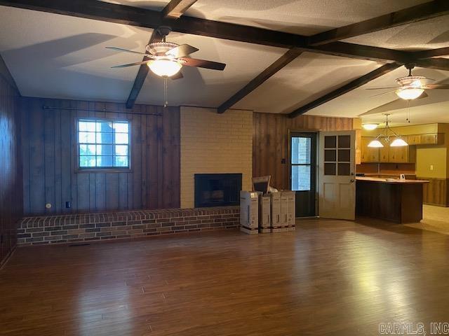 unfurnished living room featuring ceiling fan, wooden walls, lofted ceiling with beams, a fireplace, and dark hardwood / wood-style floors