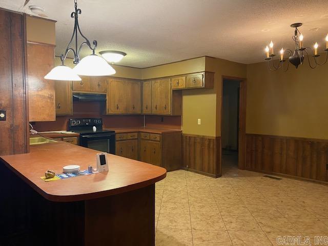 kitchen with a notable chandelier, black / electric stove, wood walls, kitchen peninsula, and decorative light fixtures