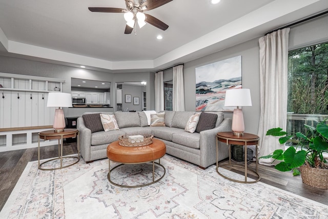 living room with a raised ceiling, ceiling fan, and hardwood / wood-style flooring