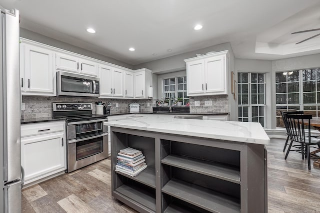 kitchen featuring hardwood / wood-style flooring, tasteful backsplash, light stone counters, white cabinetry, and stainless steel appliances