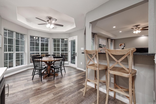 dining area with ceiling fan, a raised ceiling, and dark wood-type flooring