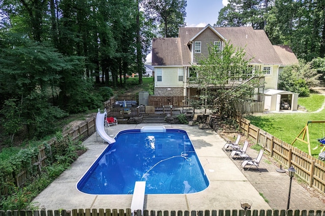 view of pool with a diving board, a water slide, a patio, and a shed