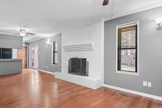 unfurnished living room with ceiling fan, ornamental molding, light wood-type flooring, and a brick fireplace