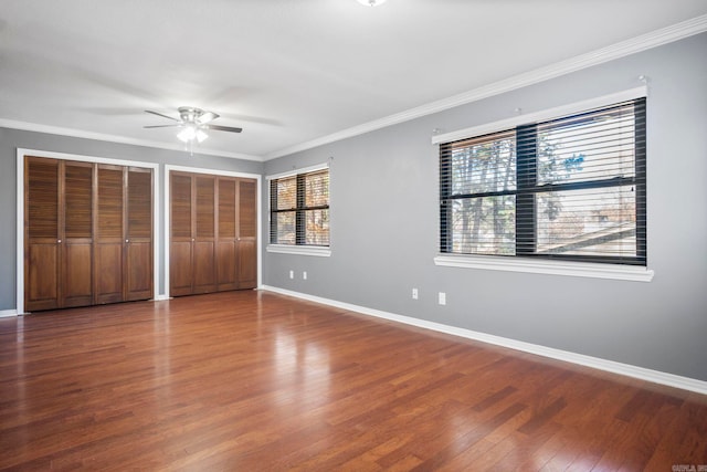 unfurnished bedroom featuring ceiling fan, ornamental molding, multiple windows, and two closets