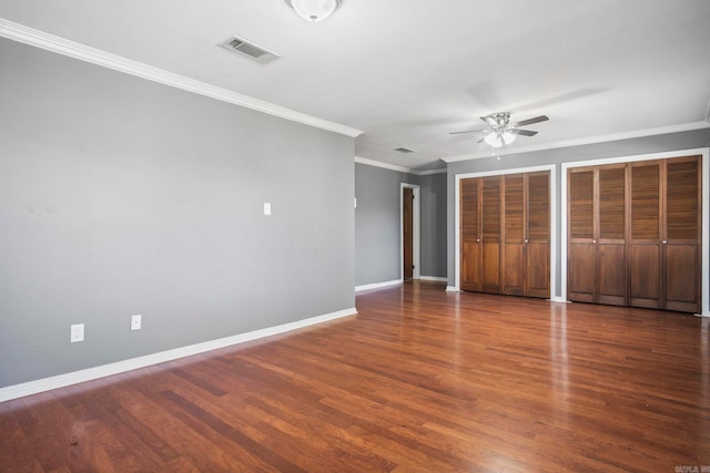 unfurnished bedroom with ceiling fan, dark hardwood / wood-style floors, crown molding, and multiple closets