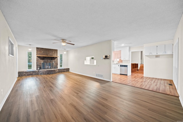 unfurnished living room featuring a stone fireplace, ceiling fan, a textured ceiling, and hardwood / wood-style flooring