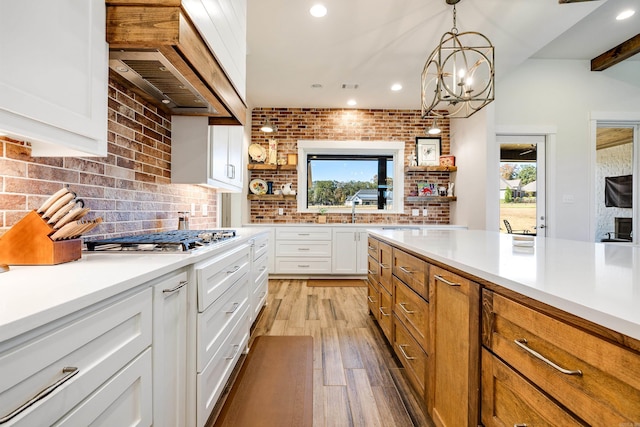 kitchen with stainless steel gas stovetop, light hardwood / wood-style flooring, decorative light fixtures, white cabinetry, and a chandelier