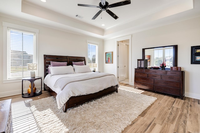 bedroom with light wood-type flooring, a tray ceiling, ceiling fan, and ornamental molding