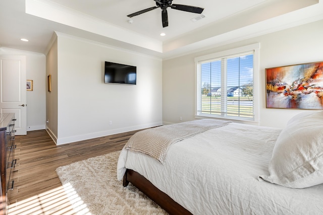 bedroom with hardwood / wood-style flooring, a raised ceiling, ceiling fan, and ornamental molding