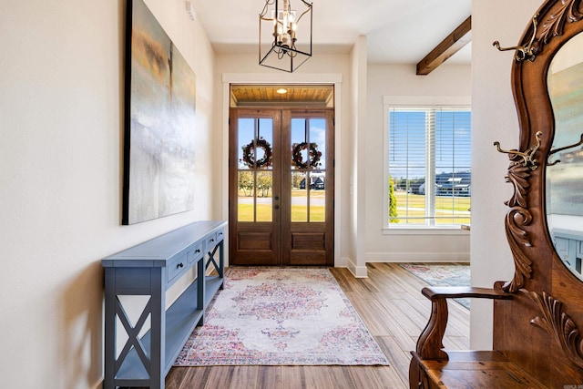 foyer entrance with french doors, beamed ceiling, a chandelier, and light hardwood / wood-style flooring