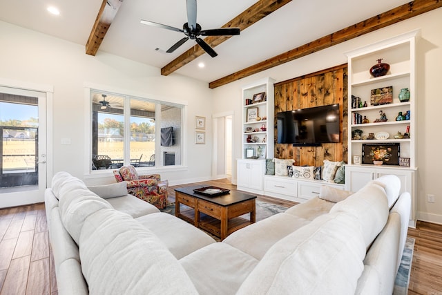 living room featuring built in features, beamed ceiling, and light hardwood / wood-style floors